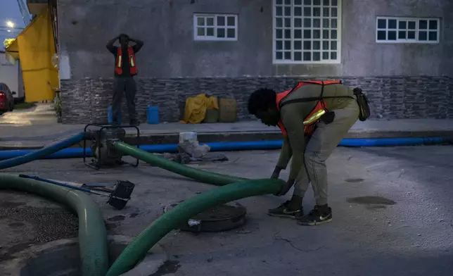 Haitian migrant Henry Chelcy, front, works to pump away sewage-infused flood water in Valle de Chalco, State of Mexico, Monday, Sept. 9, 2024. (AP Photo/Felix Marquez)