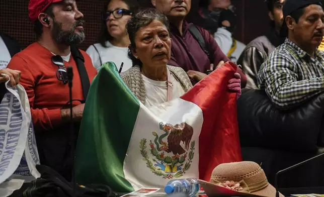 A protestor holds a Mexican flag after demonstrators broke into a Senate session in which lawmakers were debating the government's proposed judicial reform, which would make judges stand for election, in Mexico City, Tuesday, Sept. 10, 2024. (AP Photo/Felix Marquez)