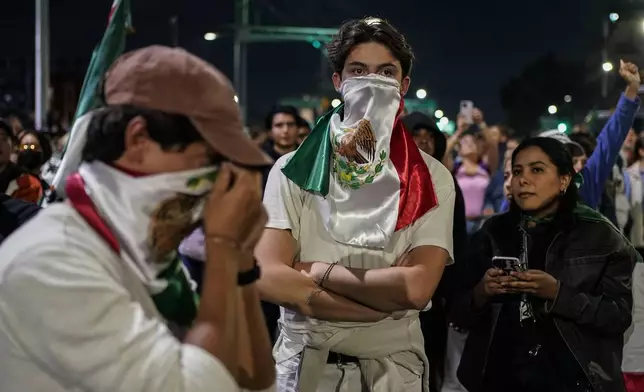 Two students cover their faces with the Mexican flag during a protest against government's proposed judicial reform, which would make judges stand for election, outside the Senate in Mexico City, Tuesday, Sept. 10, 2024. (AP Photo/Felix Marquez)