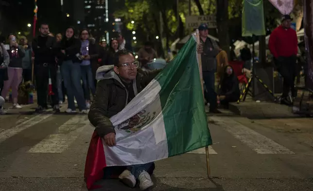 A man carrying a Mexican flag watches the senators' vote on a large screen during a protest against government's proposed judicial reform, which would make judges stand for election, outside the Senate in Mexico City, Tuesday, Sept. 10, 2024. (AP Photo/Felix Marquez)