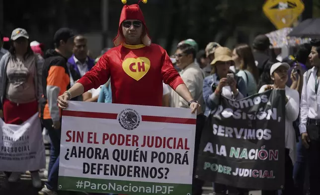 Judicial worker Jorge Reyes, wearing a Chapulín Colorado costume, holds a sign that reads in Spanish: "Without judicial power, who will be able to defend us now?" outside the Senate to protest the judicial reform bill in Mexico City, Thursday, Sept. 5, 2024, the day after Congress passed legislation that would require all judges to stand for election. (AP Photo/Felix Marquez)