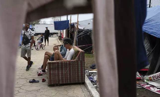 FILE - Framed by clothing hanging to dry, Venezuelan migrants sit on a sofa at a tent encampment set up near the North Bus Station in Mexico City, June 27, 2024. (AP Photo/Marco Ugarte, File)