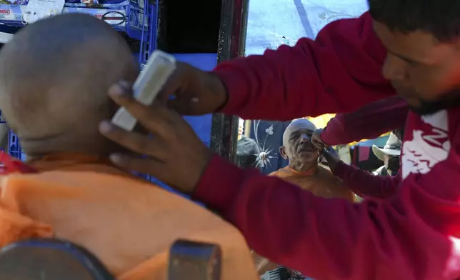 A Venezuelan migrant shaves a fellow migrant at a tent encampment set up on the perimeters surrounding the Santa Cruz y La Soledad Catholic parish church, in La Merced neighborhood of Mexico City, Monday, July 8, 2024. (AP Photo/Marco Ugarte)