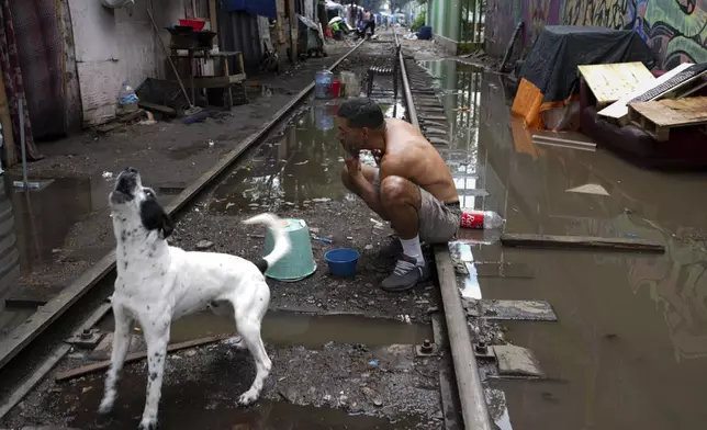 FILE - Venezuelan migrant Ali Gomez uses a bucket turned upside down to hold a compact mirror as he shaves sitting on a rail, at a migrant tent encampment set up along the Vallejo train tracks, in Mexico City, July 18, 2024. (AP Photo/Marco Ugarte, File)