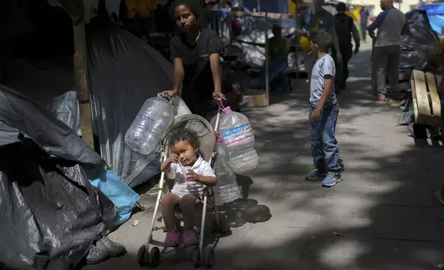 A Central American youth carries plastic containers as she goes to fetch water at a migrant tent encampment set up on the plaza of the Santa Cruz y La Soledad Catholic parish church, in La Merced neighborhood of Mexico City, Monday, July 8, 2024. (AP Photo/Marco Ugarte)