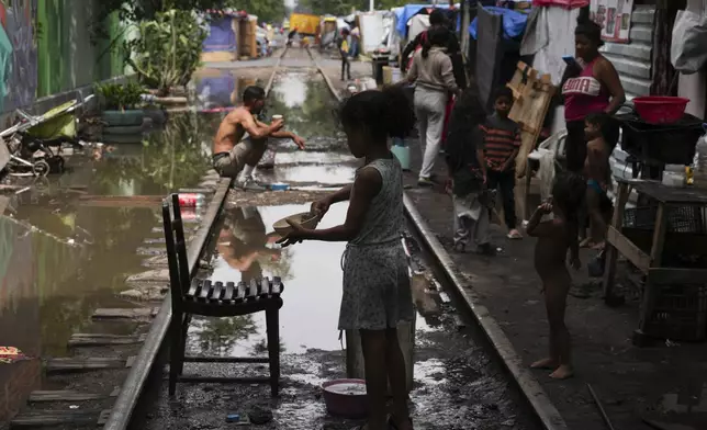 A young migrant washes a dish after heavy rains at a tent encampment set up along the Vallejo train tracks, in Mexico City, Thursday, July 18, 2024. (AP Photo/Marco Ugarte)