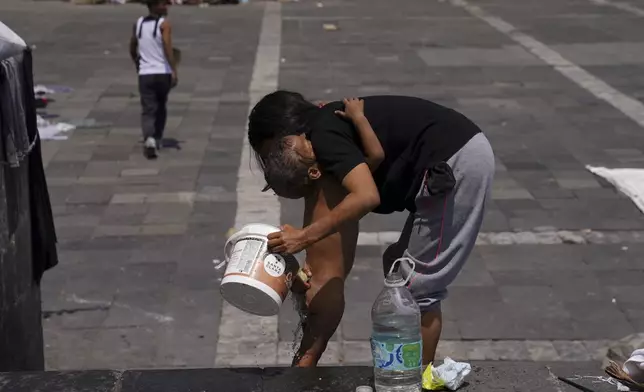 FILE - A Venezuelan migrant bathes her child at a migrant tent encampment set up on the perimeters surrounding the Santa Cruz y La Soledad Catholic parish church, in La Merced neighborhood of Mexico City, July 16, 2024. (AP Photo/Marco Ugarte, File)