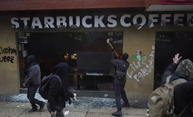 Masked youths destroy a Starbucks' storefront during a march marking the 10-year anniversary of the disappearance of 43 students from an Ayotzinapa rural teacher's college, in Mexico City, Thursday, Sept. 26, 2024. (AP Photo/Eduardo Verdugo)