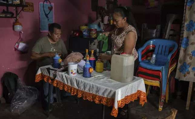 Clemente Rodríguez and Luz María Telumbre, whose son Christian is one of 43 missing students from the Raúl Isidro Burgos Rural Normal School bottle mezcal at home in Tixtla, Guerrero state, Mexico, to sell in the capital, Sunday, Aug. 25, 2024. (AP Photo/Felix Marquez)