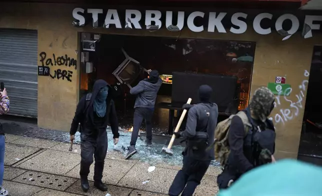 Masked youth destroy a Starbucks storefront during a march marking the 10-year anniversary of the disappearance of 43 students from an Ayotzinapa rural teacher's college, in Mexico City, Thursday, Sept. 26, 2024. (AP Photo/Eduardo Verdugo)