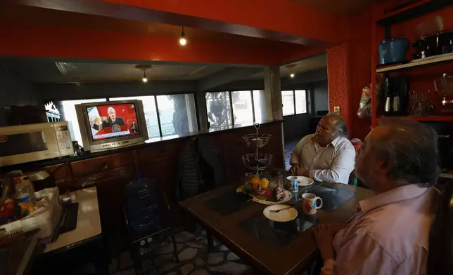 FILE - Rafael Silva, right, and his brother Gustavo watch a live broadcast of Mexican President Andres Manuel Lopez Obrador's morning press conference in Rafael's kitchen in Ciudad Nezahualcoyotl, Mexico state, on the outskirts of Mexico City, Dec. 18, 2020. (AP Photo/Rebecca Blackwell, File)