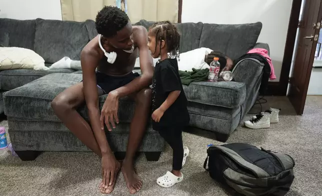 Arial Smith, left, talks with his little sister Amira, while their brother Armond sleeps on the couch at home in Lansing, Mich., Tuesday, Sept. 3, 2024. (AP Photo/Paul Sancya)