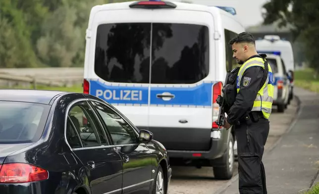 An armed German police officer checks the details of a French car near the border to Belgium in Aachen, Germany, Monday, Sept. 16, 2024, as Germany begins carrying out checks at all its land borders. (AP Photo/Martin Meissner)