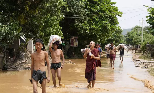 Local residents and a Buddhist monk carrying food wade through a flooded road in Naypyitaw, Myanmar, Saturday, Sept. 14, 2024. (AP Photo/Aung Shine Oo)