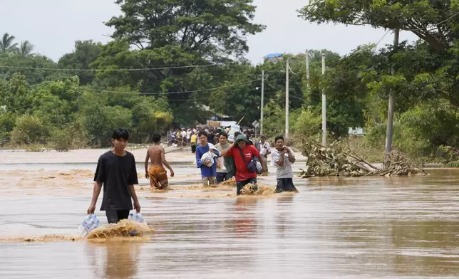 Local residents carrying food wade through a flooded road in Naypyitaw, Myanmar, Saturday, Sept. 14, 2024. (AP Photo/Aung Shine Oo)