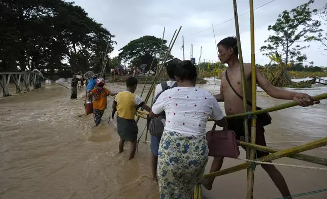 Local residents wade through flooded water at a broken bridge, in Naypyitaw, Myanmar, Tuesday, Sept. 17, 2024. (AP Photo/Aung Shine Oo)