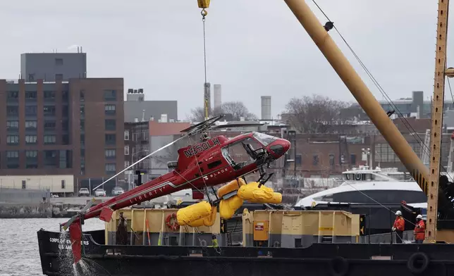 FILE - A helicopter is hoisted by crane from the East River onto a barge in New York on Monday, March 12, 2018. (AP Photo/Mark Lennihan, File)