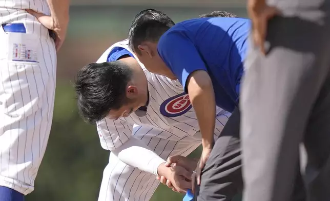 A member off the Chicago Cubs medical staff examines Seiya Suzuki's right hand and wrist after Suzuki was hit by Washington Nationals catcher Drew Millas' throw to second as Suzuki stole the base during the eighth inning of a baseball game Friday, Sept. 20, 2024, in Chicago. (AP Photo/Charles Rex Arbogast)