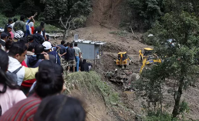 People watch earthmovers removing automobile debris and the dead bodies of victims trapped under a landslide caused by heavy rains in Kathmandu, Nepal, Sunday, Sept. 29, 2024. (AP Photo/Sujan Gurung)