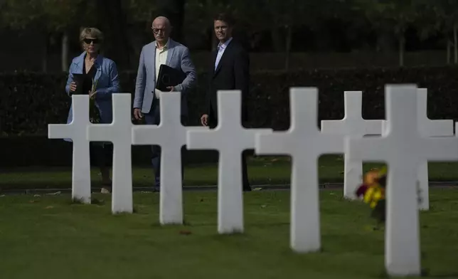 Eighty years after the liberation of the south of the Netherlands, Scott Taylor, right, Ton Hermes, center, and Maria Kleijnen, left, walk to the grave of Scott's grandfather Second Lt. Royce Taylor, a bombardier with the 527 Bomb Squadron, at the Netherlands American Cemetery in Margraten, southern Netherlands, on Wednesday, Sept. 11, 2024. (AP Photo/Peter Dejong)