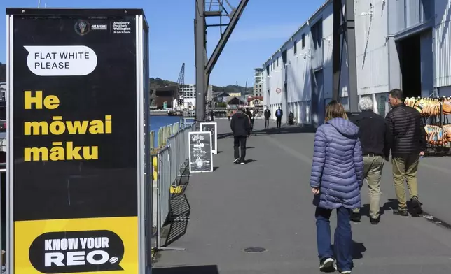 People walk past a sign encouraging them to order a coffee in Maori, during annual Maori language week in Wellington, New Zealand, Wednesday, Sept. 18, 2024. (AP Photo/Charlotte GrahamMcLay)