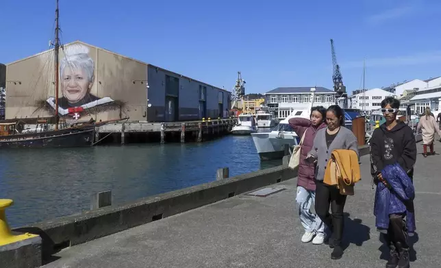 People walk on the waterfront near a mural honoring Maori leader Whae June Te Raumange Jackson as New Zealand celebrates its annual Maori language week in Wellington, New Zealand, Wednesday, Sept. 18, 2024. (AP Photo/Charlotte GrahamMcLay)