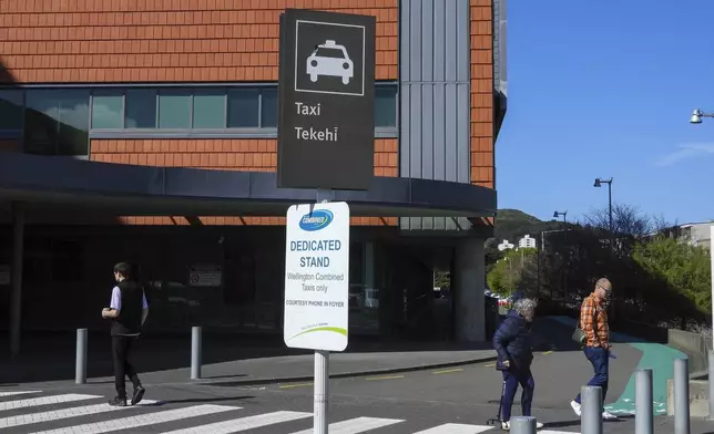 People cross a road near a taxi stand written in English and Maori languages as New Zealand celebrates its annual Maori language week in Wellington, New Zealand, Wednesday, Sept. 18, 2024. (AP Photo/Charlotte GrahamMcLay)