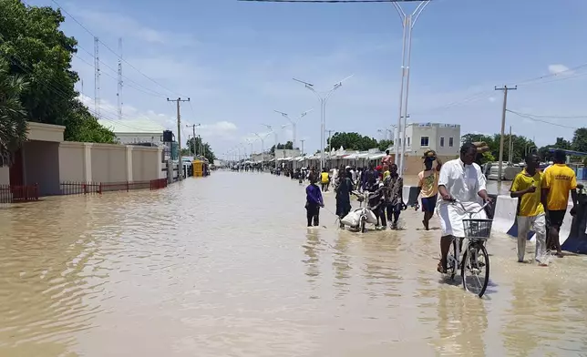 People walk through floodwaters following a dam collapse in Maiduguri, Nigeria, Tuesday Sept 10, 2024. (AP Photos/ Joshua Olatunji)