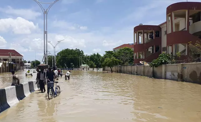 People walk through floodwaters following a dam collapse in Maiduguri, Nigeria, Tuesday Sept 10, 2024. (AP Photos/ Joshua Olatunji)