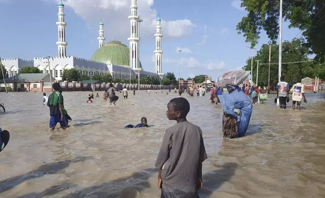 People walk through floodwaters following a dam collapse in Maiduguri, Nigeria, Tuesday Sept 10, 2024. (AP Photos/ Joshua Olatunji)