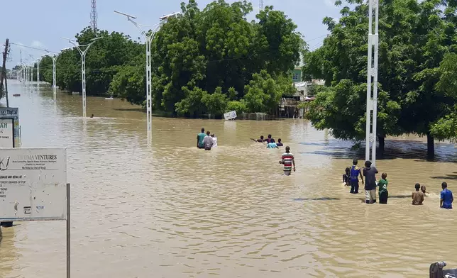 People walk through floodwaters following a dam collapse in Maiduguri, Nigeria, Tuesday Sept 10, 2024. (AP Photos/ Joshua Olatunji)