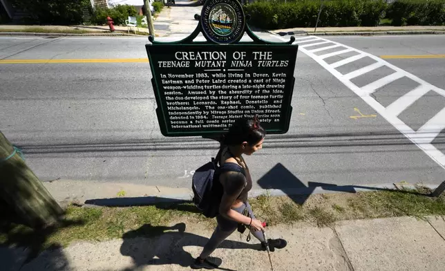 Heather Shingleton, of Dover, N.H., walks past a roadside marker honoring the local creation of the Teenage Mutant Ninja Turtles characters, Thursday, Sept. 5, 2024, in Dover. (AP Photo/Charles Krupa)