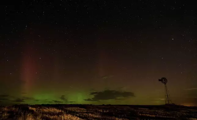 An aurora borealis, also known as the northern lights, is seen in the night sky behind a windmill water pump as lights from a passing vehicle illuminate a field on Tuesday, Sept. 24, 2024, near Washtucna, Wash. (AP Photo/Ted S. Warren)