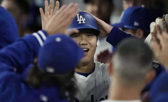 Los Angeles Dodgers' Shohei Ohtani celebrates with teammates in the dugout after hitting an RBI single and advancing to second off a throwing error by San Diego Padres right fielder Fernando Tatis Jr. during the seventh inning of a baseball game Thursday, Sept. 26, 2024, in Los Angeles. (AP Photo/Ashley Landis)