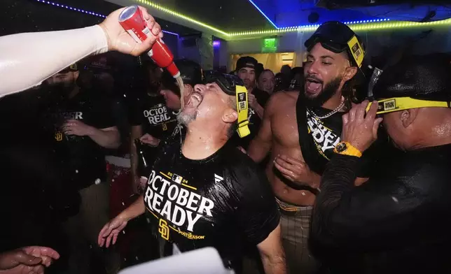 San Diego Padres pitching coach Ruben O. Niebla, center, has beer poured on him as Fernando Tatis Jr. watches after the Padres clinched a playoff spot with a triple play to end their baseball game against the Los Angeles Dodgers, Tuesday, Sept. 24, 2024, in Los Angeles. (AP Photo/Mark J. Terrill)