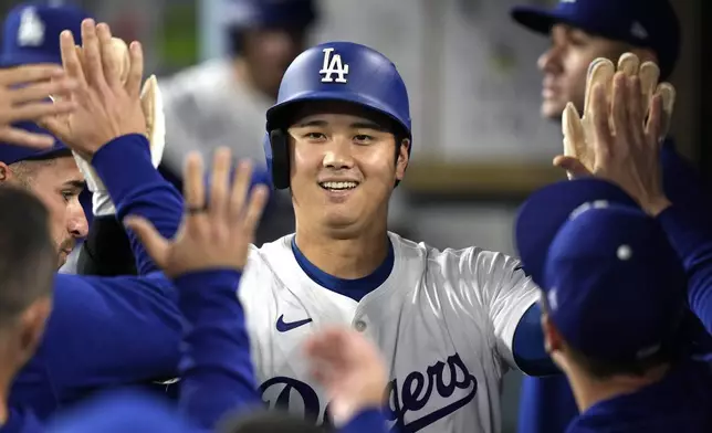 Los Angeles Dodgers' Shohei Ohtani is congratulated by teammates in the dugout after scoring on San Diego Padres shortstop Xander Bogaerts' error while trying to throw out Mookie Betts at first during the first inning of a baseball game, Tuesday, Sept. 24, 2024, in Los Angeles. (AP Photo/Mark J. Terrill)