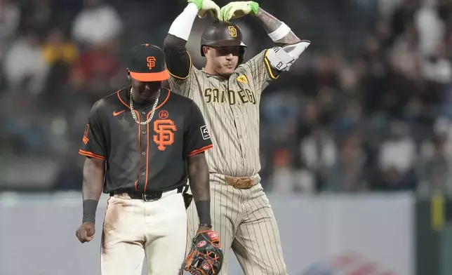 San Diego Padres' Manny Machado, right, gestures next to San Francisco Giants second baseman Marco Luciano, left, while advancing to second base after hitting a two-run single during the sixth inning of a baseball game in San Francisco, Saturday, Sept. 14, 2024. (AP Photo/Jeff Chiu)