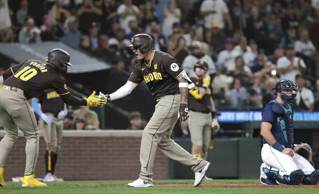 San Diego Padres' Manny Machado, center, celebrates with Jurickson Profar, left, after they scored on Machado's two-run home run as Seattle Mariners catcher Cal Raleigh, right, looks on during the sixth inning of a baseball game, Tuesday, Sept. 10, 2024, in Seattle. (AP Photo/Jason Redmond)