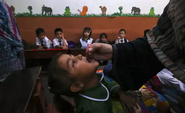 A health worker administers a polio vaccine to a child at a school in Peshawar, Pakistan, Monday, Sept. 9, 2024. (AP Photo/Muhammad Sajjad)