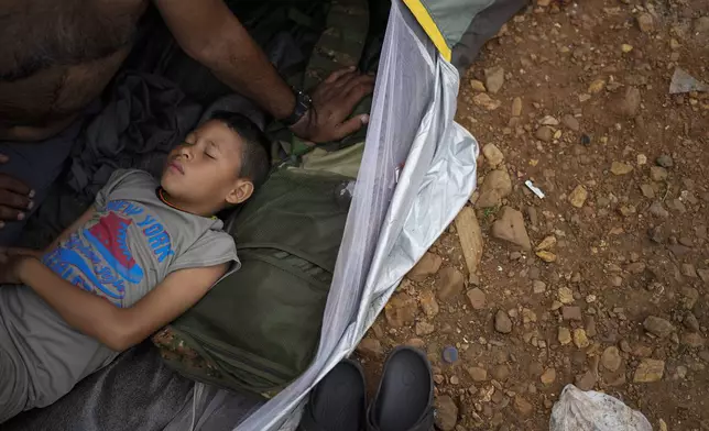 Emanuel Dordis, of Venezuela, sleeps next to his father at a camp for migrants who trekked across the Darien Gap in the hope of reaching the U.S., in Lajas Blancas, Panama, Thursday, Sept. 26, 2024. (AP Photo/Matias Delacroix)