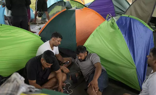 Migrants from Nepal use their phones at a camp for people who walked across the Darien Gap in hope of reaching the U.S., in Lajas Blancas, Panama, Thursday, Sept. 26, 2024. (AP Photo/Matias Delacroix)