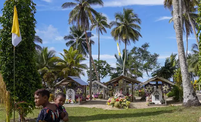 A woman and a baby walks by the cemetery of the Holy Trinity Humanistic School in Baro, near Vanimo, Papua New Guinea, Sunday, Sept. 8, 2024. Pope Francis celebrated the Catholic Church of the peripheries on Sunday as he traveled to the remote jungles of Papua New Guinea, bringing with him a ton of medicine and toys and a message of love overcoming violence for the people who live there.(AP Photo/Gregorio Borgia)