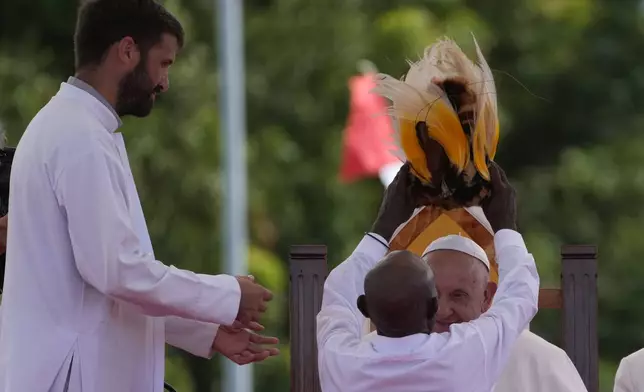 Pope Francis is greeted by Father Martin Prado, left, a missionary of the Institute of the Incarnate Word as he receives a traditional hat from a faithful in Vanimo, Papua New Guinea, Sunday, Sept. 8, 2024. . (AP Photo/Gregorio Borgia)