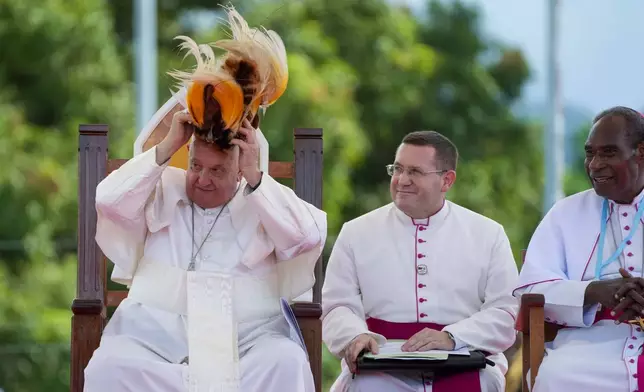 Pope Francis receives a traditional hat during a meeting with faithful in Vanimo, Papua New Guinea, Sunday, Sept. 8, 2024. Pope Francis celebrated the Catholic Church of the peripheries on Sunday as he traveled to the remote jungles of Papua New Guinea, bringing with him a ton of medicine and toys and a message of love overcoming violence for the people who live there. At right is Vanimo Bishop Francis Meli. (AP Photo/Gregorio Borgia)