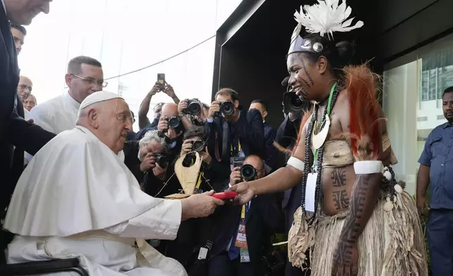 Pope Francis hands a gift to a traditional dancer as he arrives at APEC Haus in Port Moresby, Papua New Guinea, Saturday, Sept. 7, 2024. (AP Photo/Mark Baker)