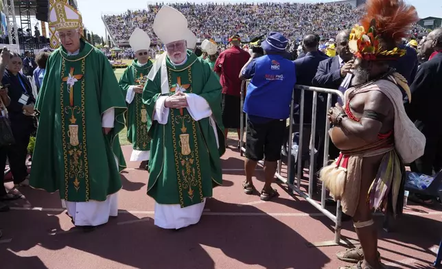 Clerics walk past a man in traditional dress as Pope Francis holds a holly mass at Sir John Guise Stadium in Port Moresby, Papua New Guinea, Sunday, Sept. 8, 2024. (AP Photo/Mark Baker)