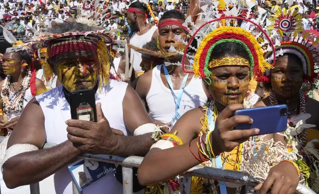 People in traditional headdress use their phones as Pope Francis holds a holly mass at Sir John Guise Stadium in Port Moresby, Papua New Guinea, Sunday, Sept. 8, 2024. (AP Photo/Mark Baker)