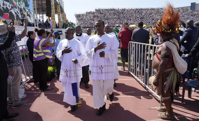 Clerics walk past a main in traditional dress as Pope Francis holds a holly mass at Sir John Guise Stadium in Port Moresby, Papua New Guinea, Sunday, Sept. 8, 2024. (AP Photo/Mark Baker)