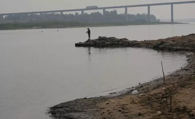 A man fishes on the shore of the Paraguay River in Mariano R. Alonso, Paraguay, Monday, Sept. 9, 2024. Water levels have plunged to their lowest-ever level amid a drought, according to Paraguay's Meteorology and Hydrology Office. (AP Photo/Jorge Saenz)