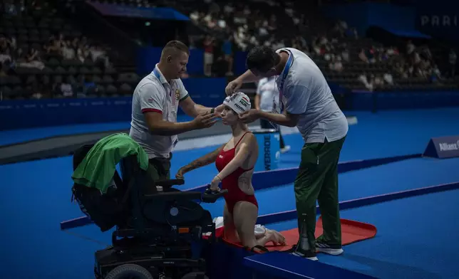 Paralympic athlete Zsanett Adami-Rozsa, of Hungary, is helped by members of her team before to enter at the swimming pool during a heats swimming serie at the 2024 Paralympics, Thursday, Aug. 29, 2024, in Paris, France. (AP Photo/Emilio Morenatti)